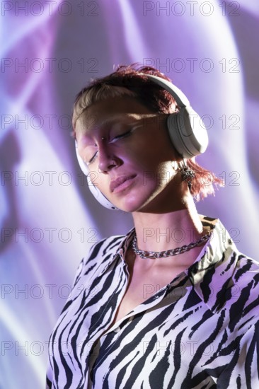 A young, trendy woman wearing headphones enjoys music. Her stylish zebra-print shirt and modern accessories reflect her unique fashion sense against a vibrant light background