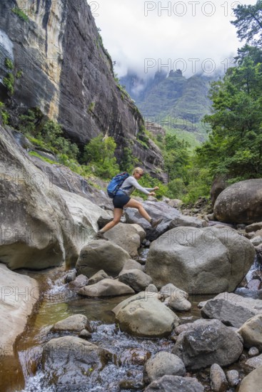 Female hiker jumping over rocks, Tugela Gorge or Tugela Gorge in the riverbed, Drakensberg National Park, KwaZulu Natal, South Africa