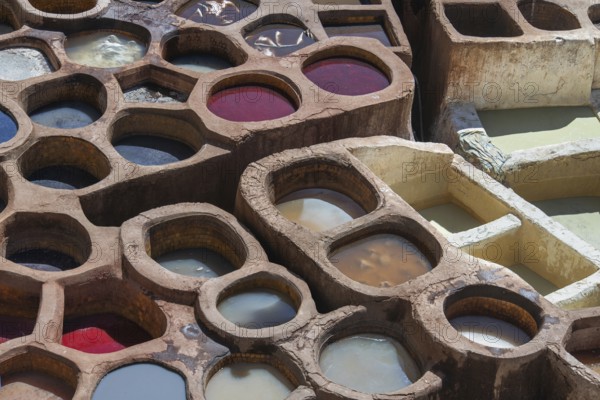 Aerial view of traditional leather tanning pits filled with vibrant dye baths in warm sunlight in Fez, Morocco. The ancient artistry showcases a stunning array of colors and textures