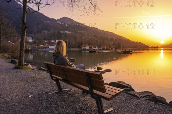 A person sitting on a bench by the lake at sunset with mountains in the background, Großer Alpsee, Immenstadt im Allgäu, Bavaria, Germany