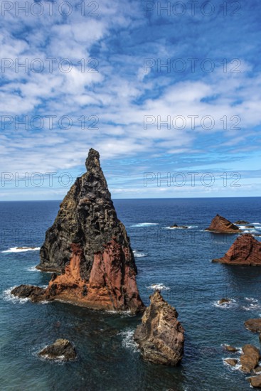 Steep rock formations rise out of the deep blue sea under a partly cloudy sky