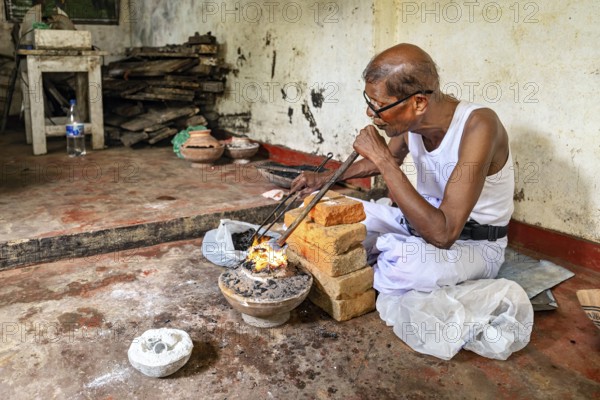 An old man works with fire and bricks in a workshop, he looks concentrated, a man burns sapphires in a small oven in the town of Ratnapura in Sri Lanka