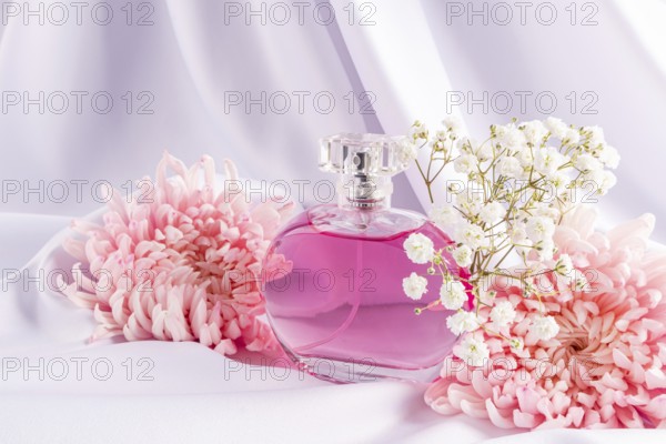 A stylish perfume bottle filled with pink liquid is elegantly nestled among pink flowers and white blossoms, set against a soft, white fabric backdrop