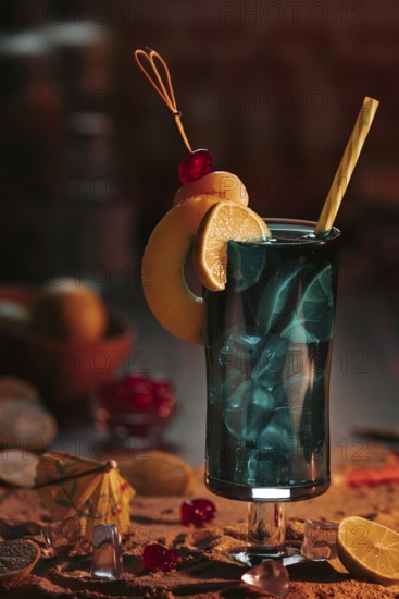 Cocktail in a glass with ice cube cubes, decorated with lime slices and cherries on a sandy background in a sunset atmosphere