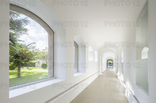 Bright corridor of hospital with arched windows fills with natural light, showcasing a serene garden view. Smooth white walls create a calm and peaceful atmosphere