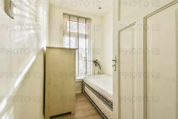 A bright and cozy room featuring a wooden cupboard and a neatly made bed, complemented by natural light streaming through the window