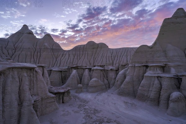 A breathtaking landscape view of the Bisti/De-Na-Zin Wilderness in New Mexico, showcasing striking eroded rock formations under a vibrant twilight sky