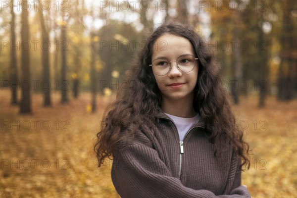 A teenage girl with curly hair enjoys a peaceful moment in an autumn forest, surrounded by golden leaves. The scene captures the serenity of the fall season