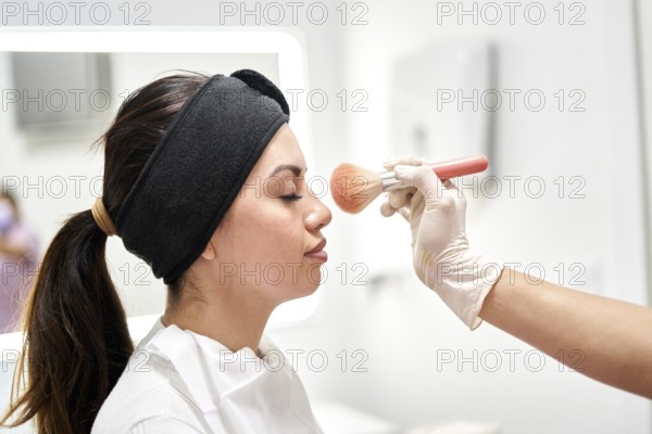 A skilled professional applies makeup to a client's face with care and precision at a beauty salon dedicated to aesthetic medicine. The ambiance is calm and inviting
