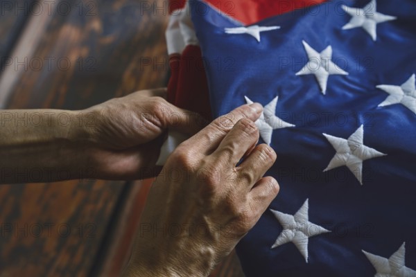 Close-up of hands reverently folding an American flag, emphasizing intricate stitching and vibrant colors. The image conveys respect, patriotism, and attention to detail