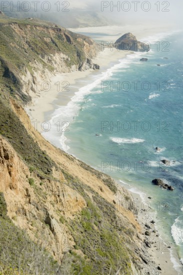 The dramatic Big Sur coastline features steep cliffs and vibrant ocean waves crashing against the shore, creating a stunning view of California's natural beauty
