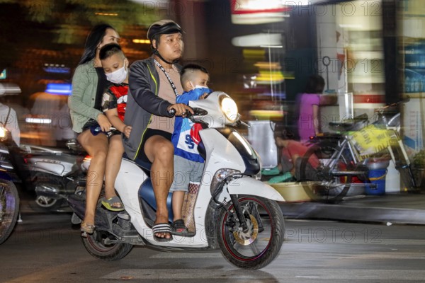 A family rides a scooter through a busy city street at night, people on scooters drive through the streets of Hanoi Vietnam