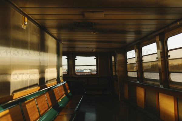 Warm sunlight illuminates the empty seats of a ferry interior, casting soft shadows in New York. The serene setting invites reflection and a sense of calm during the journey
