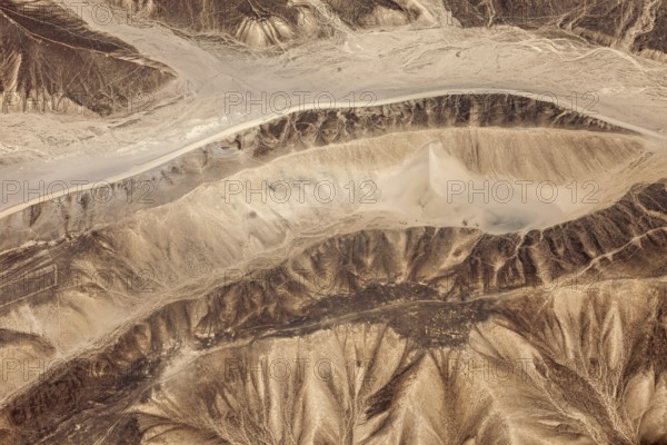Aerial view of a dry, mountainous desert landscape with sandy shades of brown, the landscape and desert near Nasca in the Andes of Peru