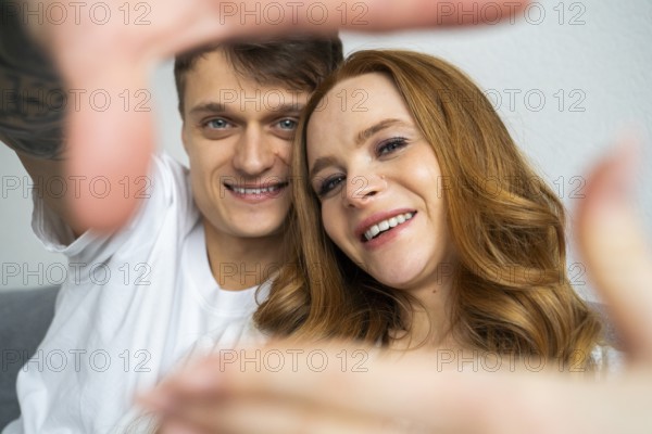 A happy couple captures a joyful moment together at home. They are smiling and relaxed, framed by their outstretched arms, symbolizing love and togetherness