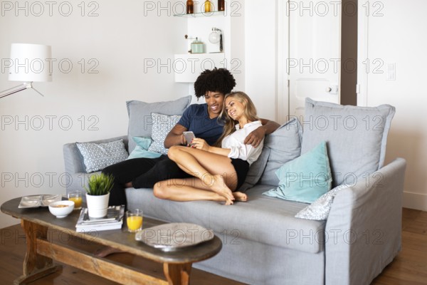 A happy couple sitting on a comfortable sofa, enjoying relaxed quality time together in a modern, light-filled living room, with drinks on the wooden table nearby