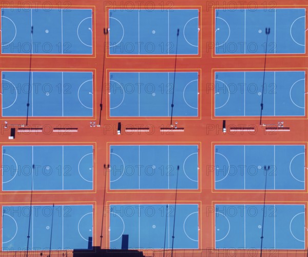 From above, this image captures a series of neatly arranged netball courts in the heart of Canberra, Australia's capital. The drone's perspective highlights the vibrant blue playing surfaces contrasted with bold orange boundaries