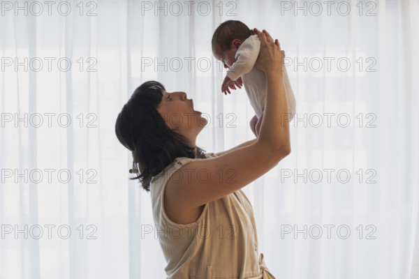 A joyful young mother holds her newborn baby lovingly in a softly lit room. This tender moment captures the essence of family love and the beginning of a new journey
