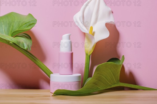Pink skincare cosmetic products displayed with lush green leaves and a white calla lily against a vibrant pink background, presenting a refreshing, natural aesthetic