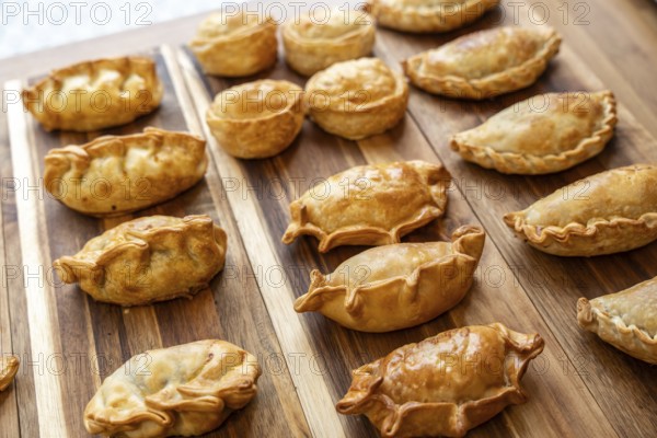 Collection of freshly baked golden brown empanadas and round savory pastries arranged on a striped wooden cutting board, showcasing delicious homemade appetizers