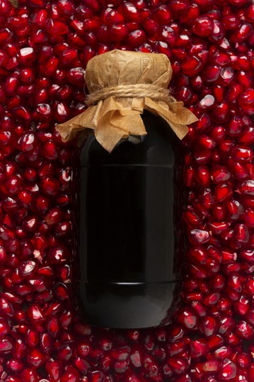 Pomegranate sauce in a bottle, top view, in pomegranate seeds, food background, vertical, no people
