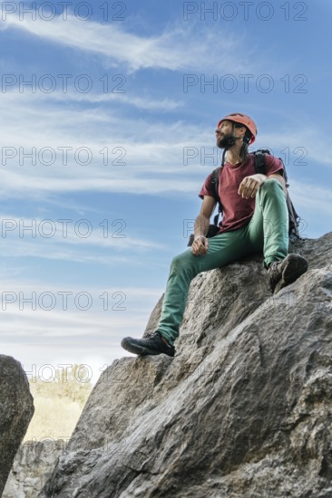 Young man with safety helmet and climbing equipment resting at the top of the mountain