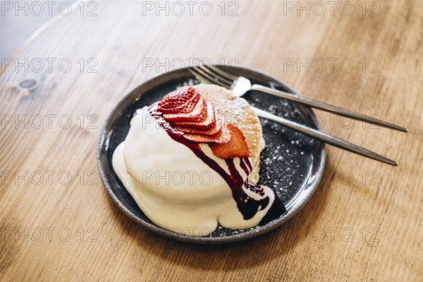 Fluffy japanese pancakes topped with fresh strawberries, a drizzle of cream, and berry sauce. Served on a dark plate, this inviting breakfast dish is perfect for food lovers