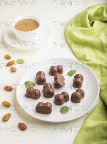Chocolate candies with almonds and a cup of coffee on a white wooden background and green textile. side view, close up