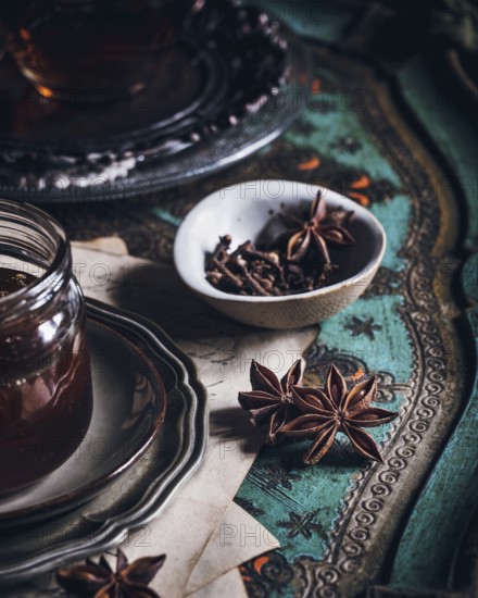 A cozy arrangement featuring a cup of tea infused with anise, presented on an ornate table. The scene includes a glass jar, star anise pods, and a delicate bowl on a vintage surface
