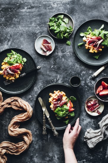 Elegant gourmet dish featuring pumpkin waffles beautifully topped with savory Iberian ham, fresh greens, and ripe tomato slices, creating a delightful balance of flavors