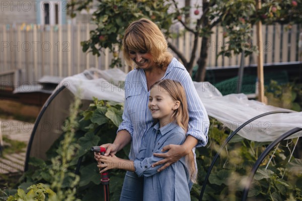 A joyful mother daughter duo tends to their greenhouse, surrounded by lush plants. They share a special bond while watering the vegetables under the warm sun