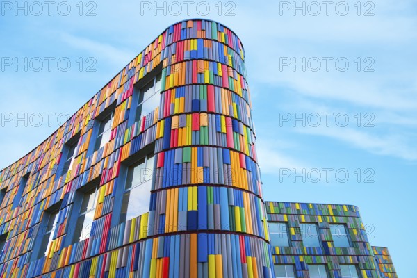 Low angle of a vibrant multicolor facade adorns a modern curved building, presenting a striking visual contrast with the clear blue sky in the background