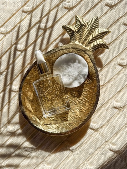 A luxurious skincare cosmetic bottle with gold flakes beside a cotton pad, resting in an ornate pineapple dish on a textured surface, exuding elegance and sophistication in the bathroom