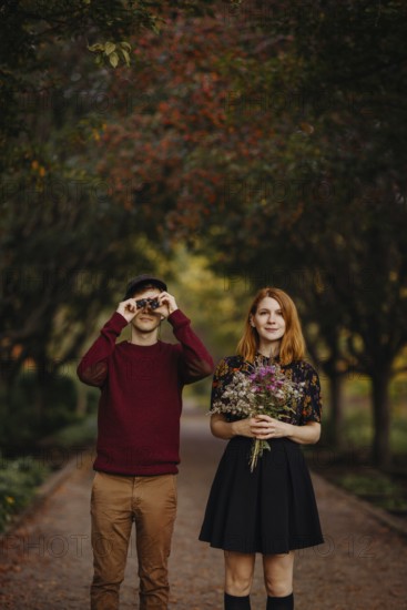 A couple enjoying a beautiful fall day in Quebec, Canada. The woman holds a bouquet of wildflowers, while the man looks through binoculars, surrounded by autumn foliage