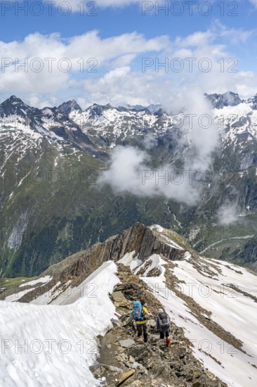 Mountaineer on a rocky ridge with snow, descent from the summit of Schönbichler Horn, view of snow-covered mountain peaks and valley Zemmgrund, Berliner Höhenweg, Zillertal Alps, Tyrol, Austria