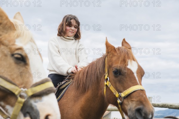 Young girl enjoying a peaceful day at the farm, sitting atop a horse. The clear sky and gentle surroundings make this a serene scene of rural life and connection with animals