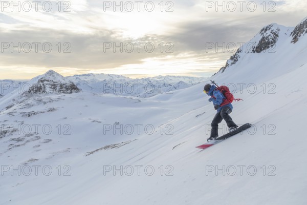 A snowboarder rides down a pristine snowy slope, surrounded by stunning alpine peaks under a soft, cloudy sky, highlighting the adventure and beauty of nature