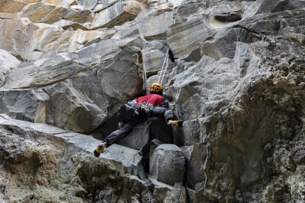 A climber in a red shirt and helmet is scaling a rugged mountain face. The image captures the essence of traditional climbing in nature, emphasizing skill and determination