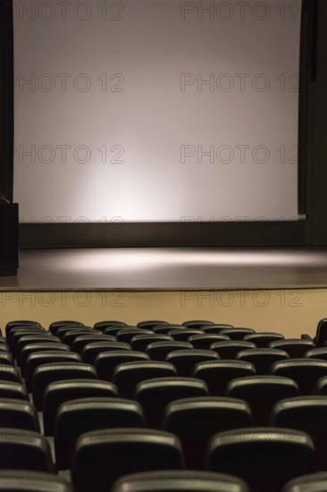 Rows of empty convention center seats facing a blank stage with a large screen, creating a quiet and expectant ambiance suitable for performances, presentations, or screenings