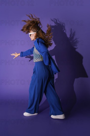 A young woman dances energetically against a vibrant purple background. Her dynamic pose and flowing hair capture a sense of freedom and movement, showcasing vibrant energy