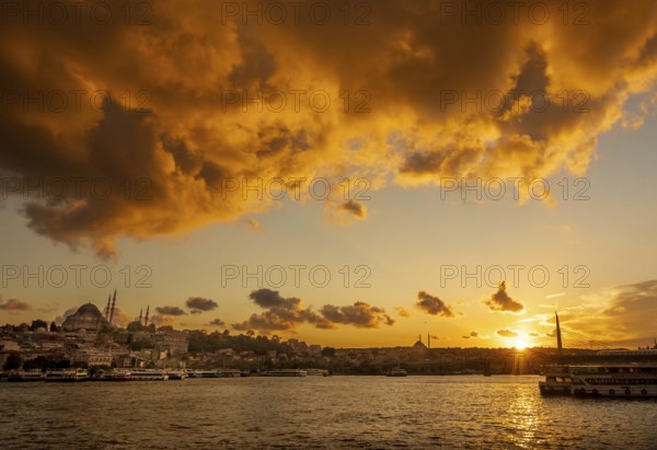 A vibrant sunset illuminates the sky above Istanbul, highlighting the silhouettes of mosques and a bridge, with the sunlight reflecting off the waters of the Bosphorus