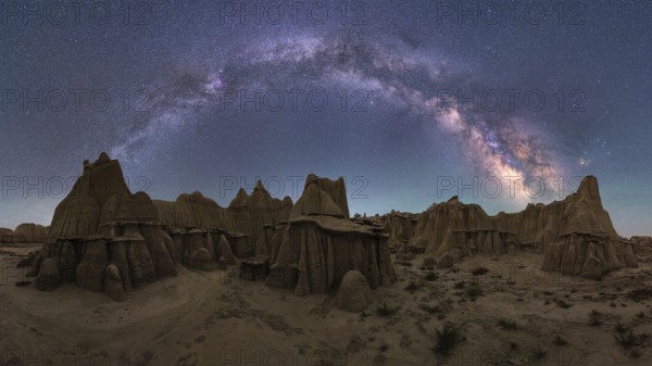Stunning view of the Milky Way arching over a rugged sandstone desert landscape in Utah, USA. The sky is brilliantly illuminated with stars, highlighting the wild scenery