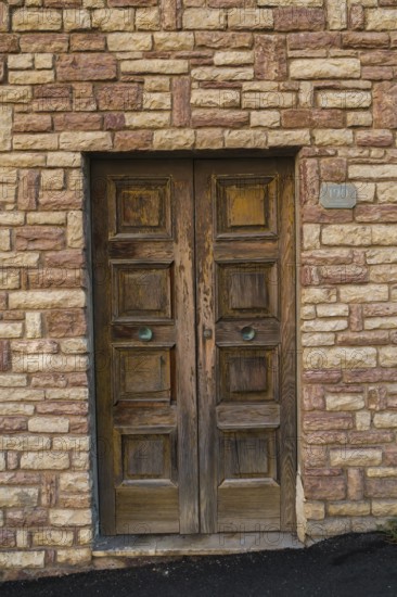 Distressed brown painted wooden entrance door on tan and beige cut stone residential building facade, Riomaggiore, Cinque Terre, La Spezia province, Italy