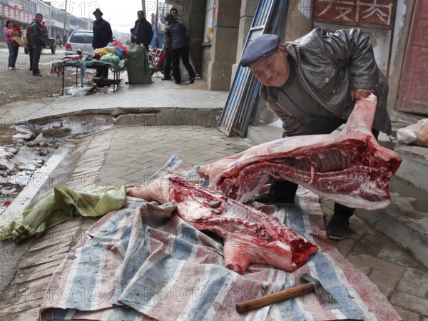 Xining, CHN, 27/02/09 - A butcher cuts up a side of pork on the pavement of a village near Xining. (, CHINA