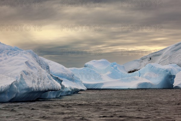 Huge, sharp icebergs stretch out under a cloudy sky as dusk falls, icebergs in the landscape of the Southern Ocean in Antarctica