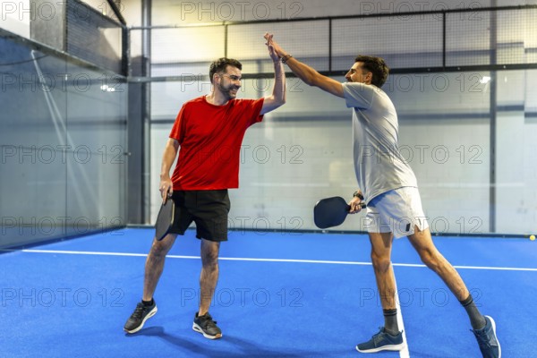 Male pickleball players celebrating victory and sportsmanship, high fiving on an indoor court after an intense game, holding paddles and sharing a moment of triumph
