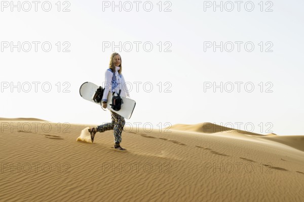 Young woman with snowboard in the sand dunes, near Merzouga, Meknès-Tafilalet region, Erg Chebbi, northern Sahara, Morocco