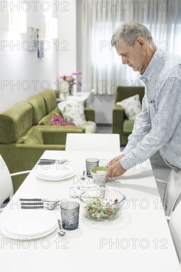 A man with intellectual disabilities carefully arranges dishes on a dining table in a supervised home. The scene captures the warmth and attention to detail in everyday tasks and home life