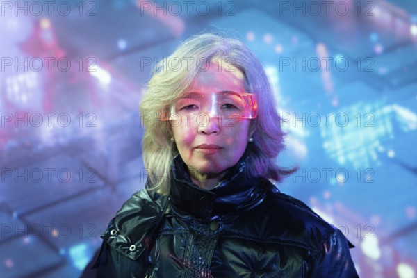An elderly Asian woman dons futuristic eyewear, fully immersing herself in the vibrant, digital world of the metaverse. Her reflective pose highlights the fusion of technology and tradition