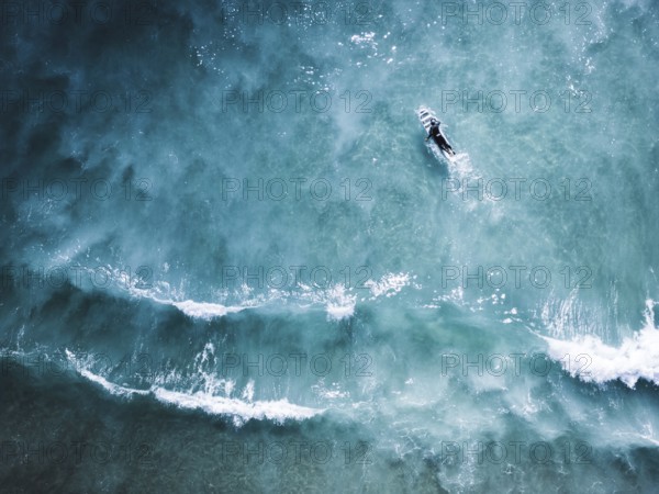 Aerial shot capturing a surfer navigating the clear blue waves of Portugal. The image emphasizes the natural beauty and dynamic motion of the ocean landscape
